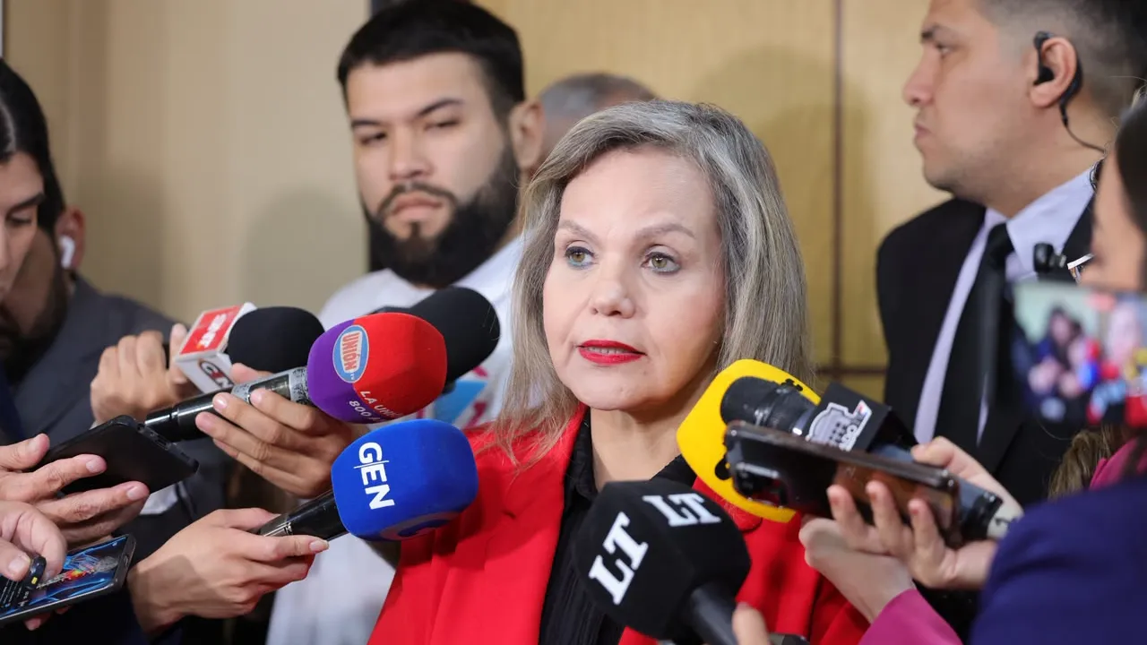 Lilian Samaniego con saco rojo habla rodeada de micrófonos de prensa durante una rueda de prensa en el Congreso.