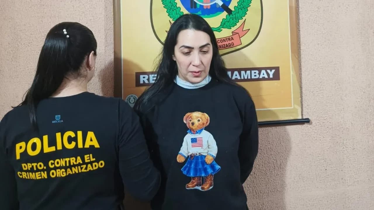 Mujer detenida con buzo negro junto a una agente policial del departamento contra el crimen organizado.