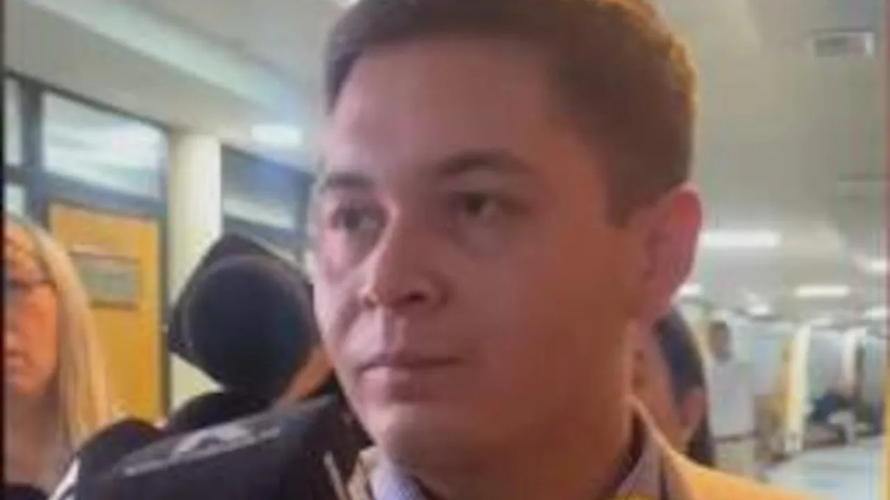 Hombre de saco claro habla ante micrófonos de prensa en un pasillo institucional