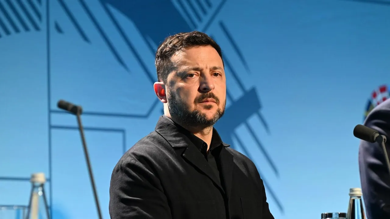 Volodimir Zelensky observa con expresión seria durante una conferencia con micrófonos frente a un fondo azul.