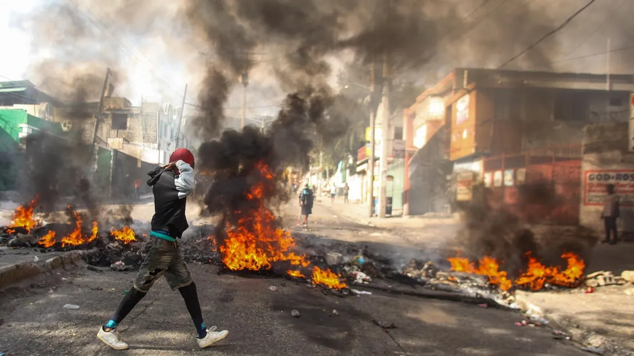 Una persona camina frente a barricadas de neumáticos en llamas que desprenden un humo denso sobre una calle urbana.