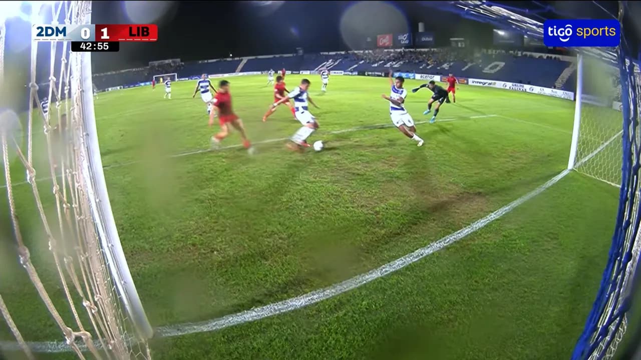 Jugadores disputan el balón en el área chica cerca del arco durante una confusa jugada de gol nocturna.