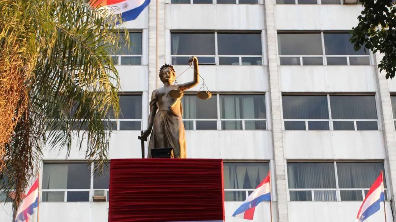 Estatua de la Justicia frente a la fachada del Palacio de Justicia con banderas paraguayas.