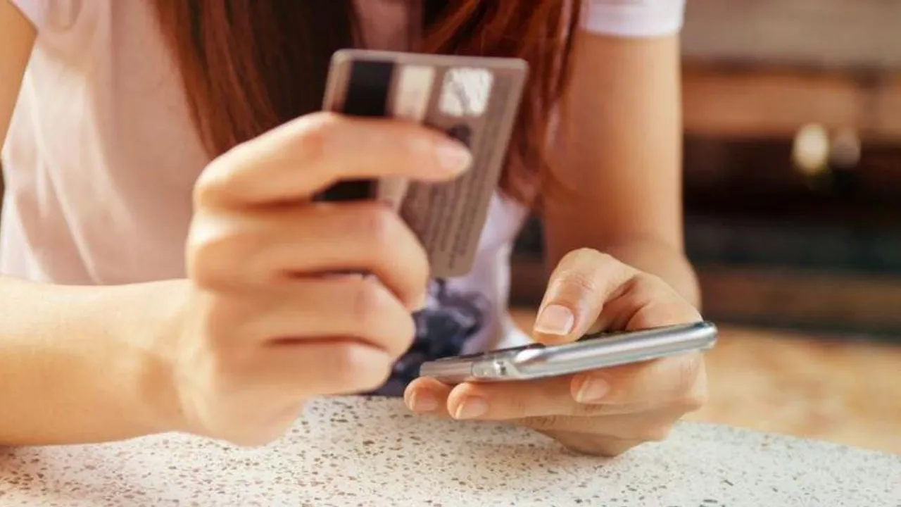 Manos de una mujer sosteniendo una tarjeta bancaria plástica mientras digita información en un teléfono inteligente.