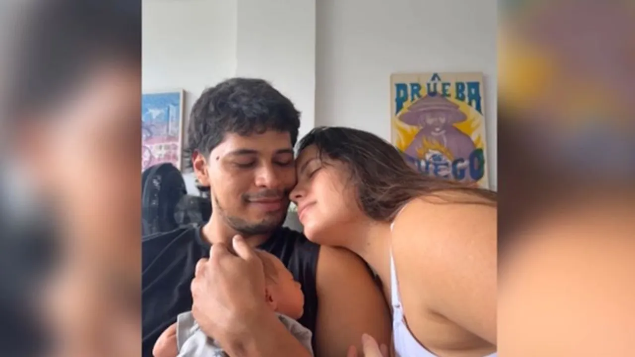 Un hombre sonriente abraza a su pareja y sostiene con ternura a su pequeño bebé recién nacido en su regazo.