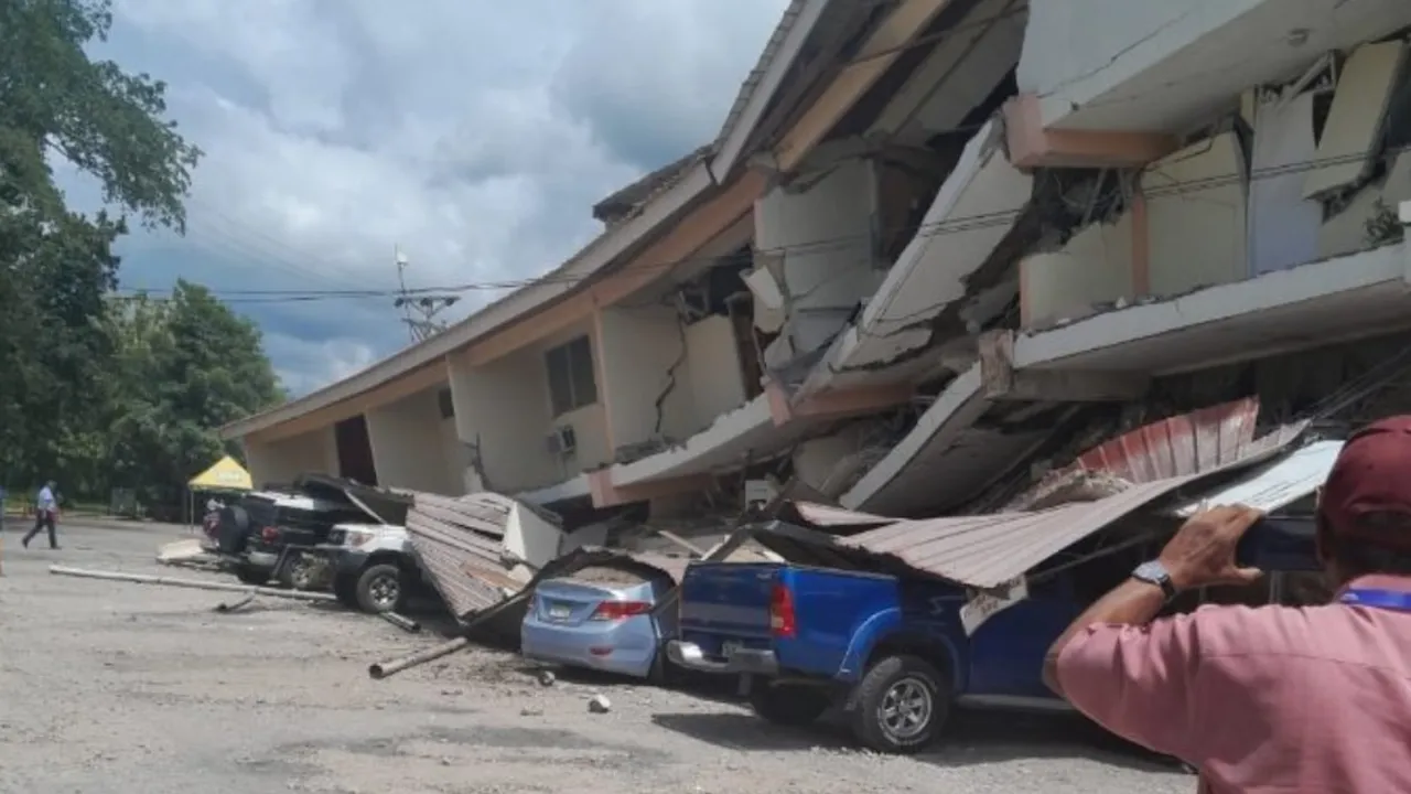 Edificio de dos pisos parcialmente derrumbado sobre varios vehículos estacionados tras un sismo.