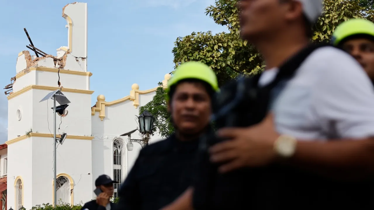 Estructura de una iglesia con graves grietas y derrumbe en la torre tras un sismo con personal de seguridad al frente.