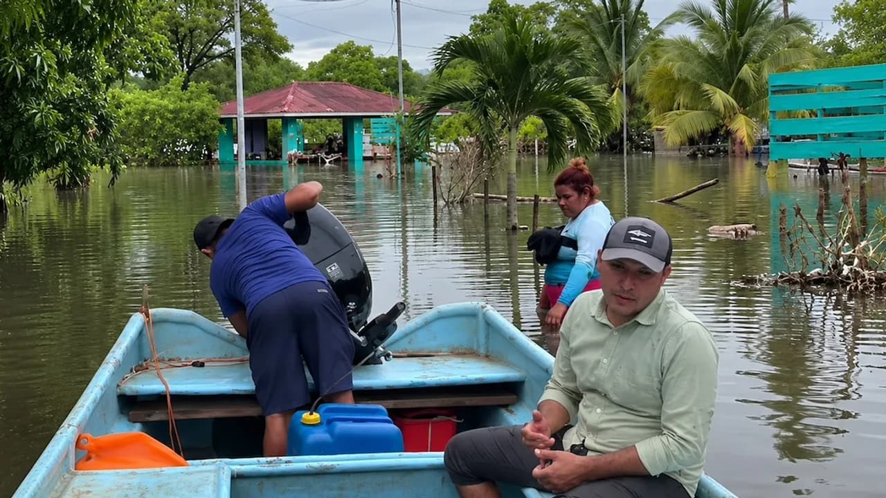 Pobladores se desplazan en una lancha azul sobre calles inundadas frente a viviendas y palmeras.