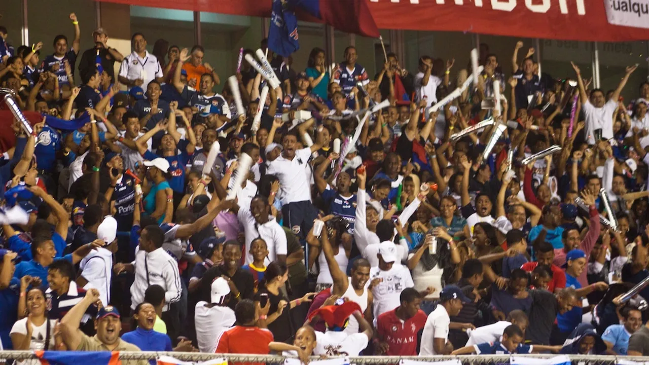 Multitud de aficionados en las gradas de un estadio agitando varas inflables y celebrando durante un evento deportivo