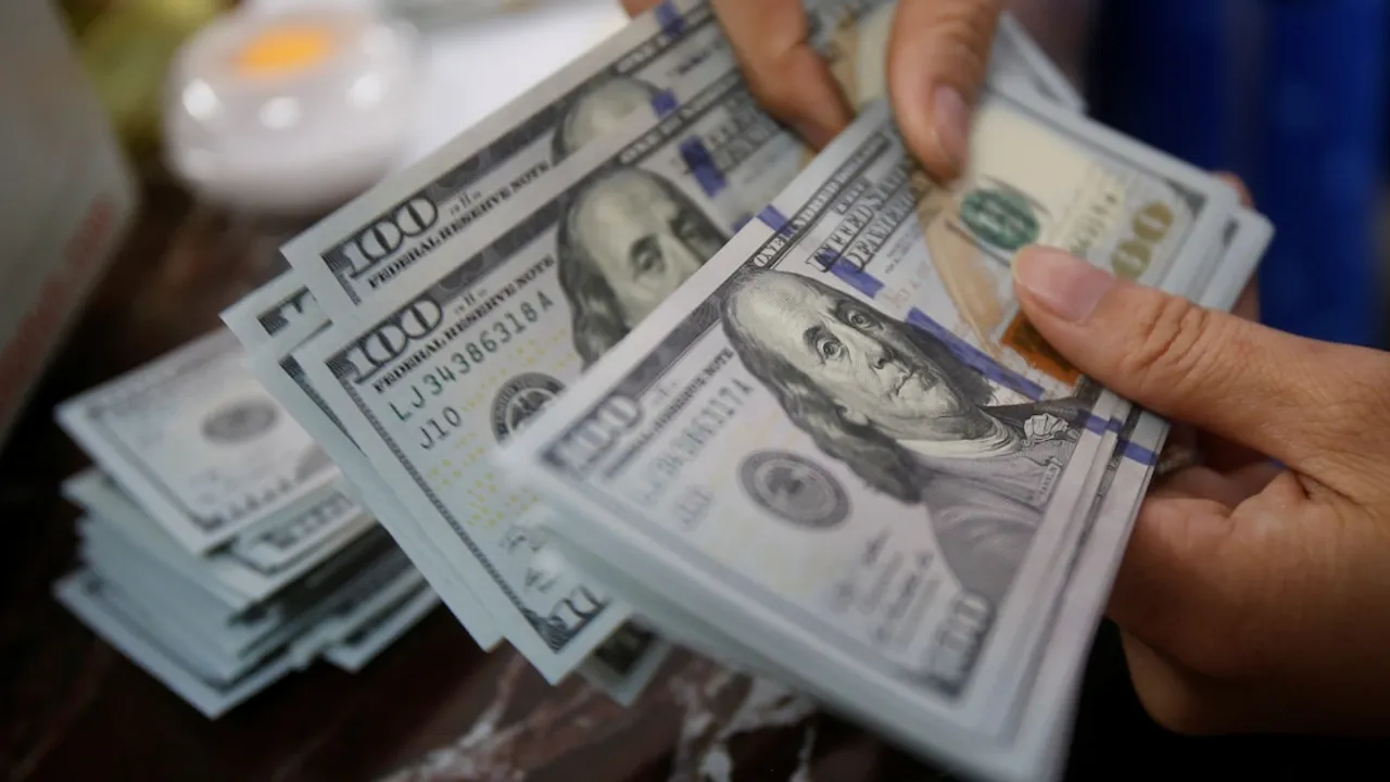 Manos de una persona contando un fajo de billetes de cien dólares estadounidenses sobre una mesa.