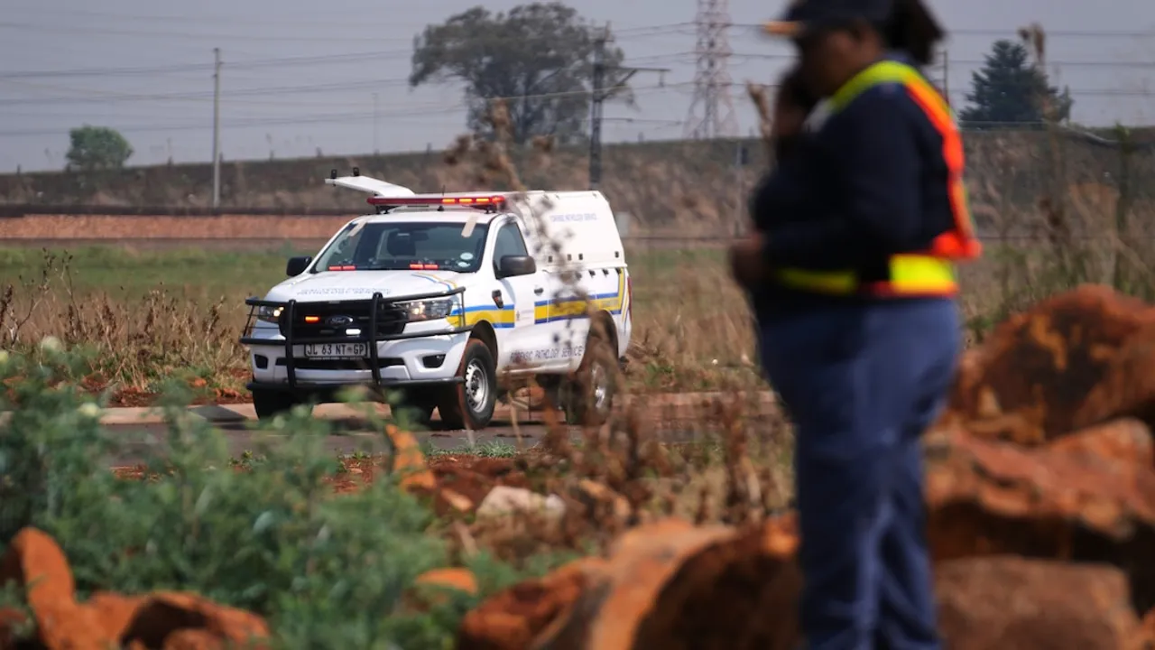 Camioneta blanca del servicio forense policial de Sudáfrica circulando por un camino rural con luces encendidas.