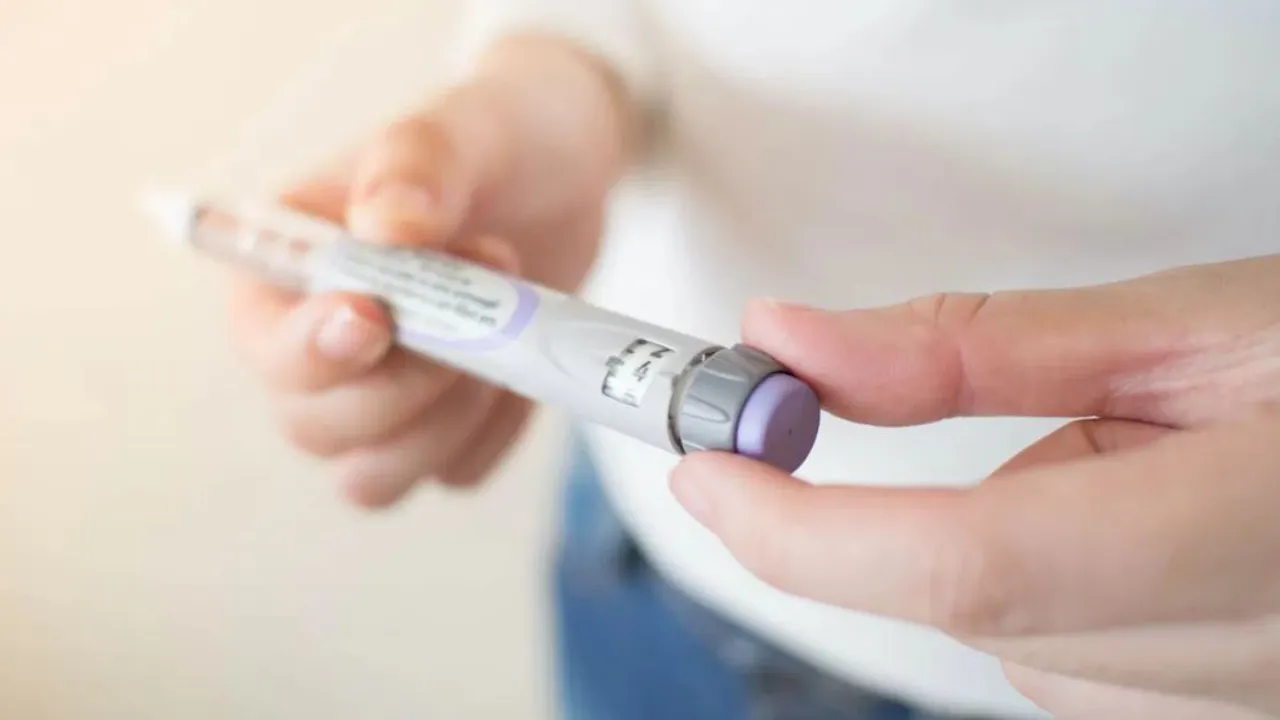 Persona sosteniendo un dispositivo inyectable en forma de lapicera para aplicar medicación subcutánea.