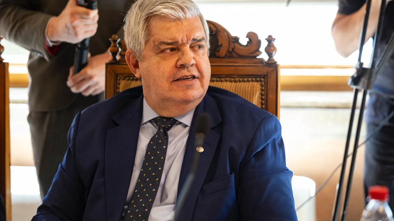 Enrique Riera vestido con traje azul y corbata durante una conferencia oficial sentado frente a un micrófono