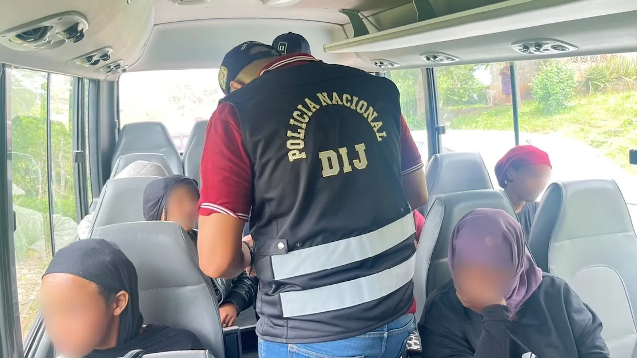 Agente policial de espaldas inspecciona a varios pasajeros sentados dentro de un vehículo de transporte.
