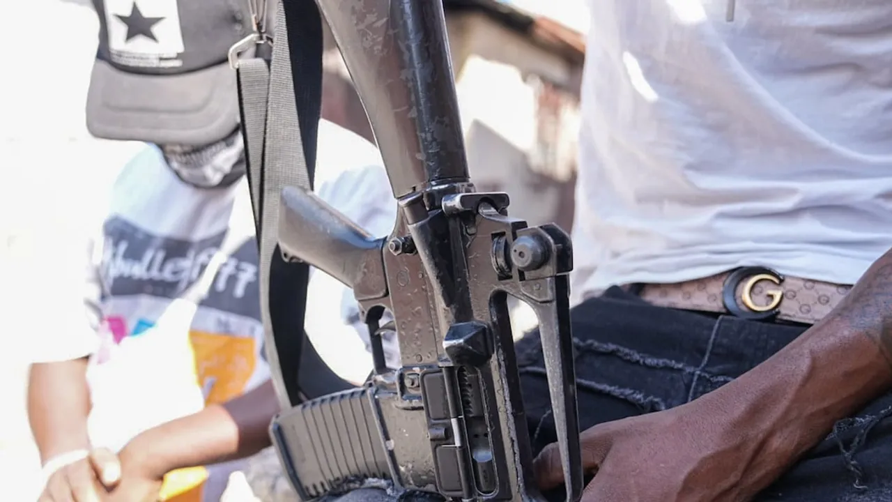 Primer plano de un fusil de asalto sostenido por un hombre con ropa informal en una zona urbana
