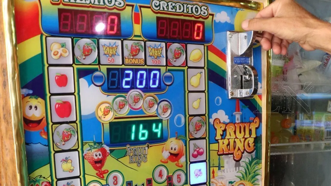 Mano introduciendo una moneda en la ranura de una máquina de tragamonedas con luces y figuras de frutas.