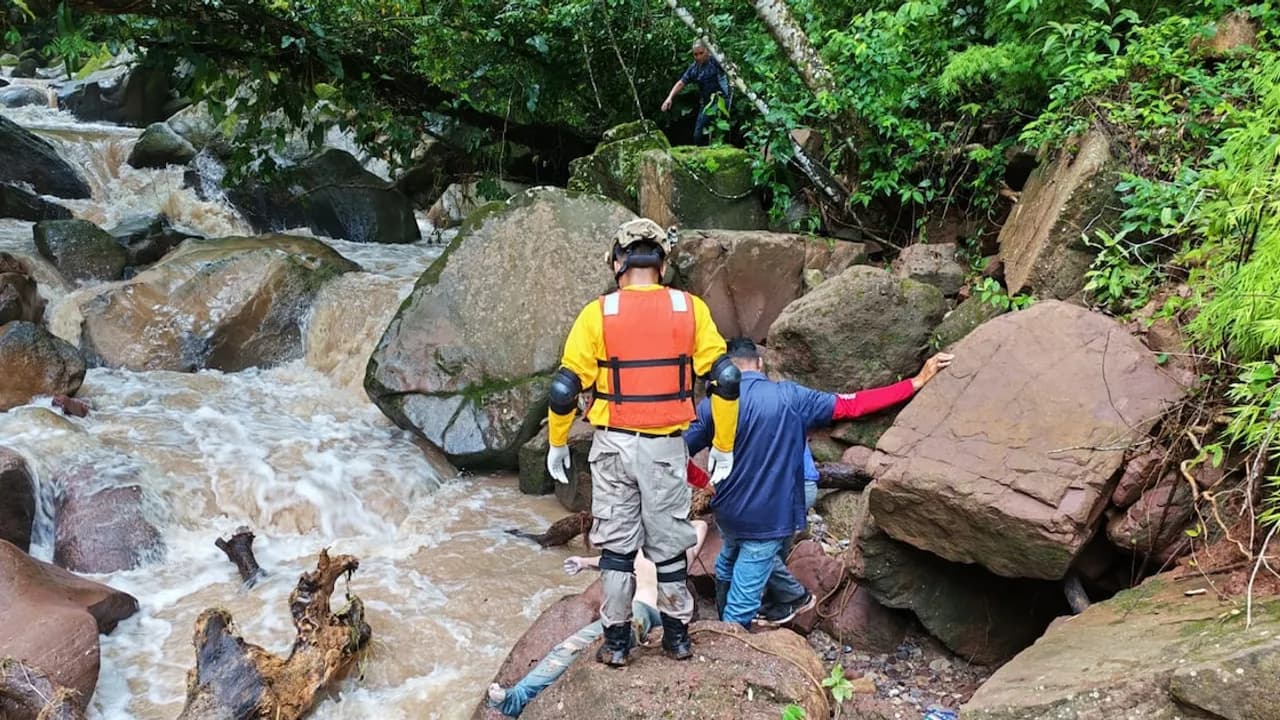 Rescatistas con chalecos salvavidas inspeccionan rocas y aguas turbulentas en un río montañoso durante una búsqueda.