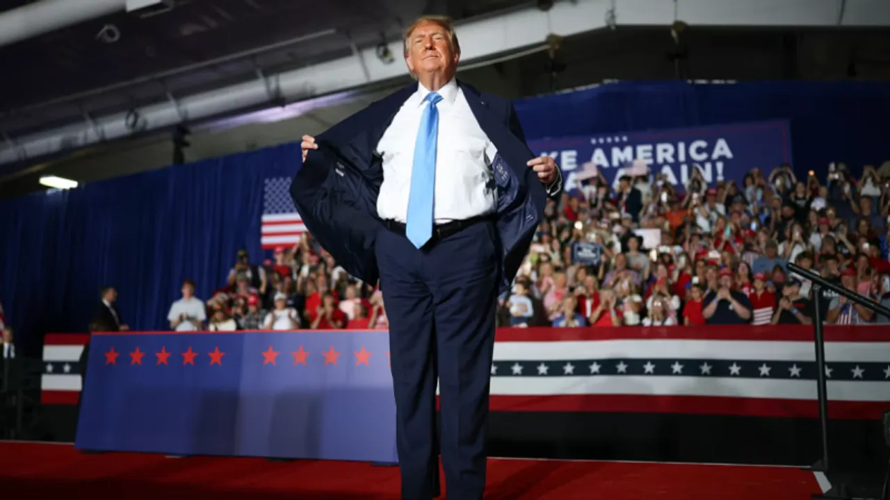 Donald Trump sobre un escenario abre su saco azul marino mostrando el forro ante una multitud con banderas