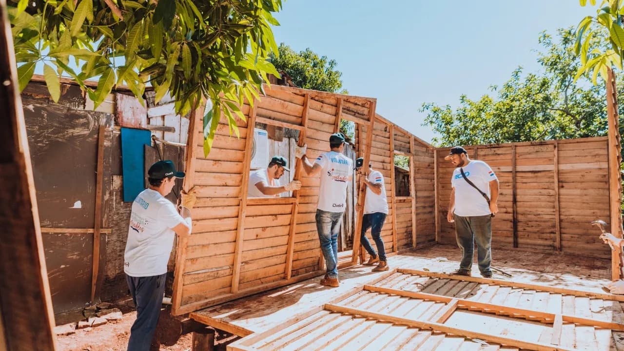 Grupo de jóvenes voluntarios levantando paneles de madera durante la construcción de una vivienda social.