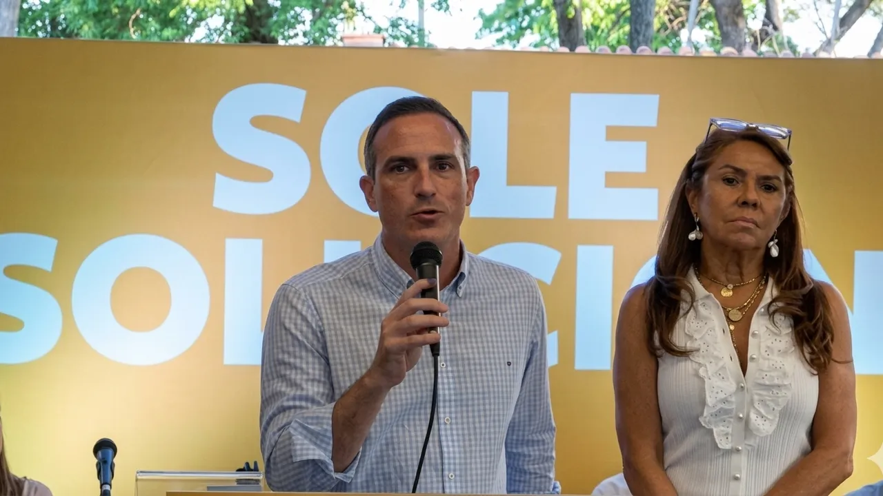 Stephan Rasmussen y Celeste Amarilla frente a un cartel amarillo durante una conferencia de prensa institucional.