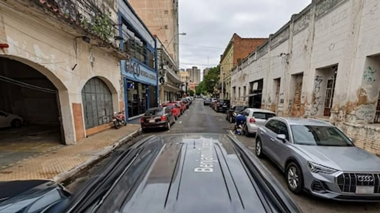 Calle angosta del microcentro con vehículos estacionados y calzada reducida frente a edificios antiguos.