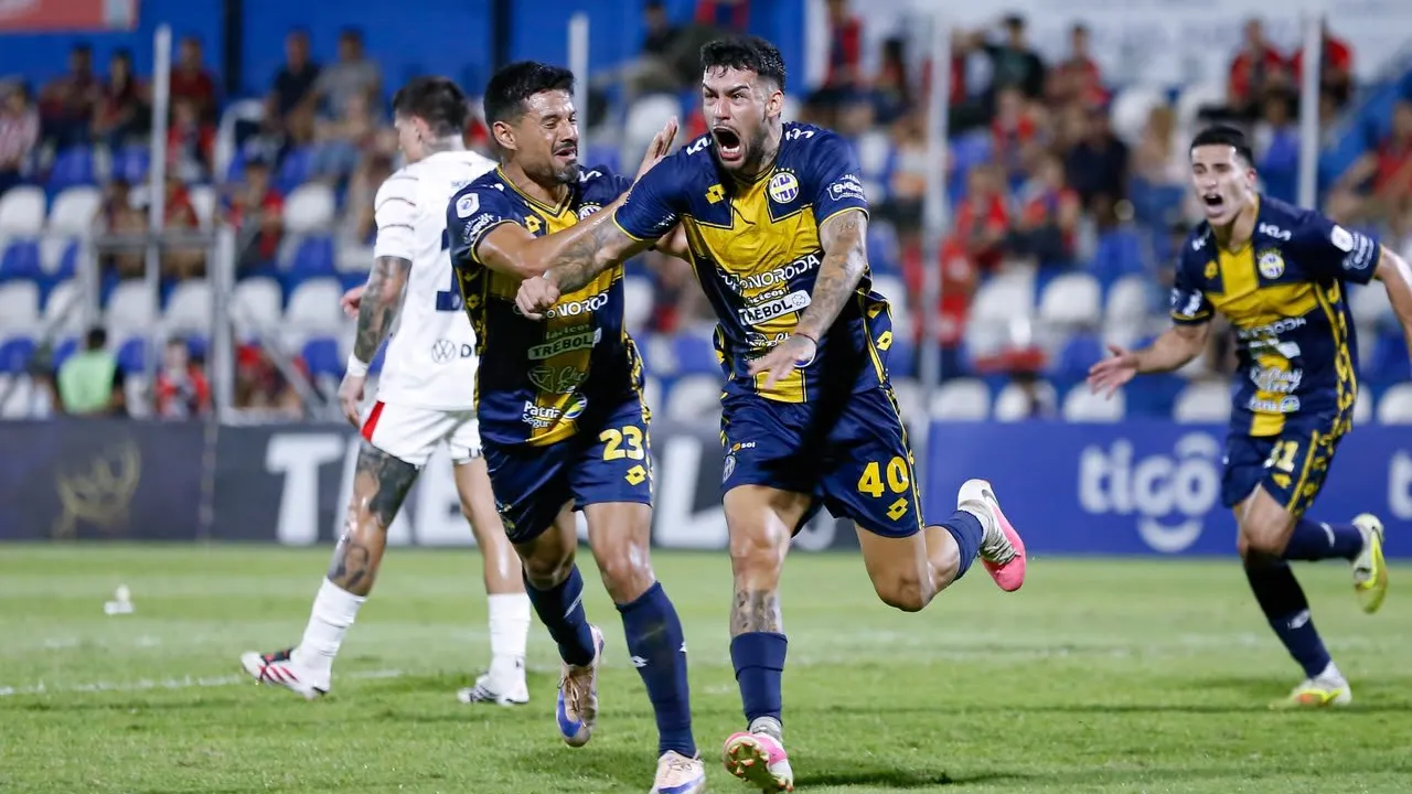 Futbolista con camiseta azul y oro festeja eufórico gritando con los brazos abiertos junto a sus compañeros
