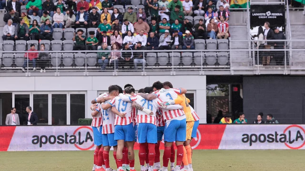 Futbolistas de la selección paraguaya abrazados en ronda previa sobre el césped frente a las gradas.