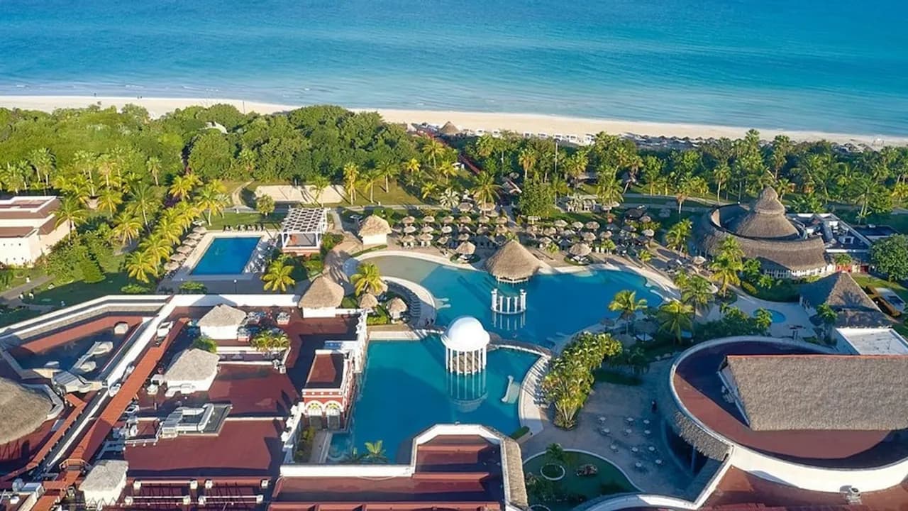 Complejo hotelero frente al mar con piscinas amplias, sombrillas de paja y costa de arena blanca en Cuba.