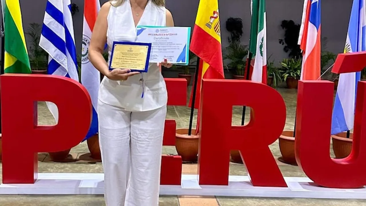 Mujer con traje blanco sostiene una placa dorada y un certificado frente a las letras de Perú