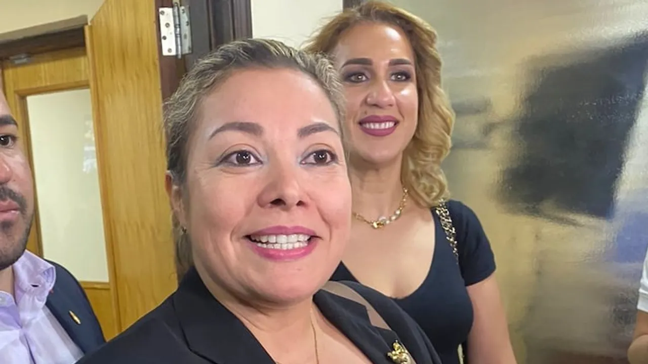 La senadora Zenaida Delgado sonríe en primer plano junto a Fátima Agüero en un pasillo institucional.