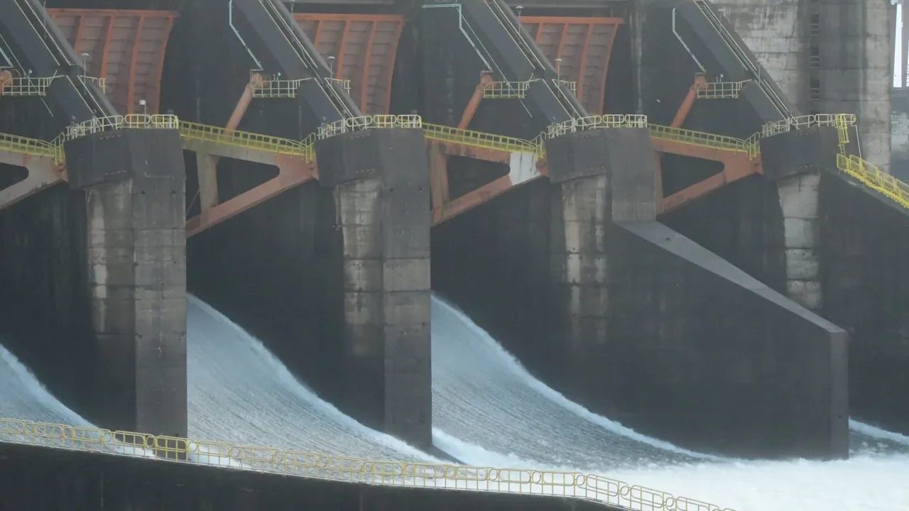 Compuertas de la represa vertiendo intensos chorros de agua espumosa a través de canaletas de concreto.