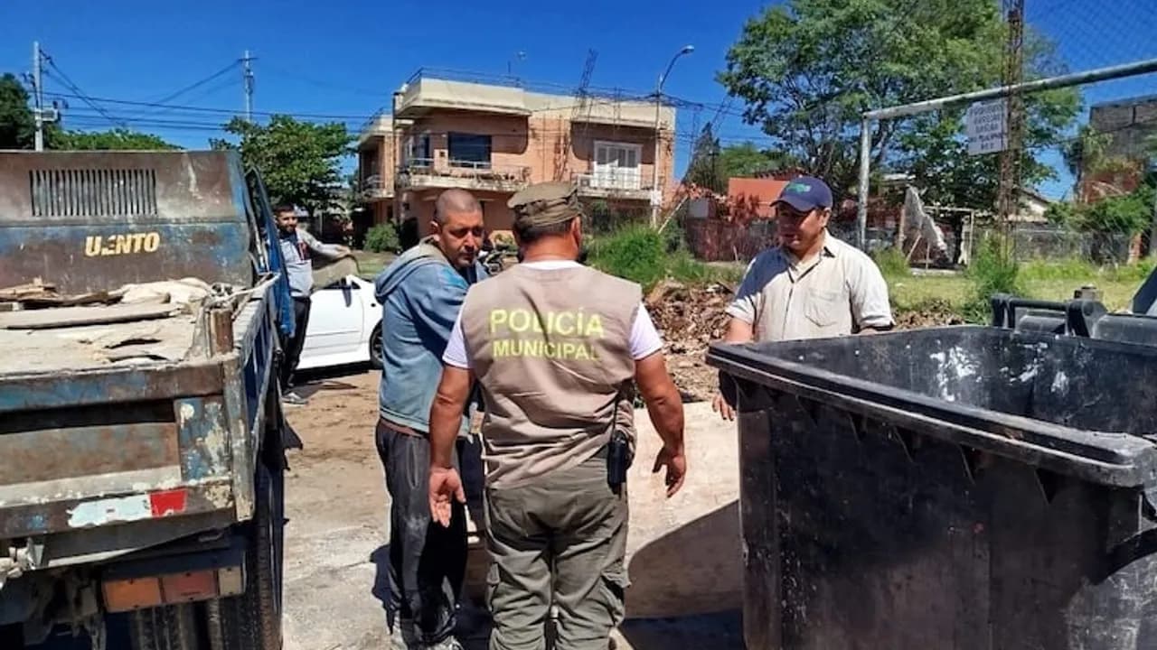 Un inspector de la Policía Municipal habla con dos hombres cerca de un contenedor de basura y un camión.