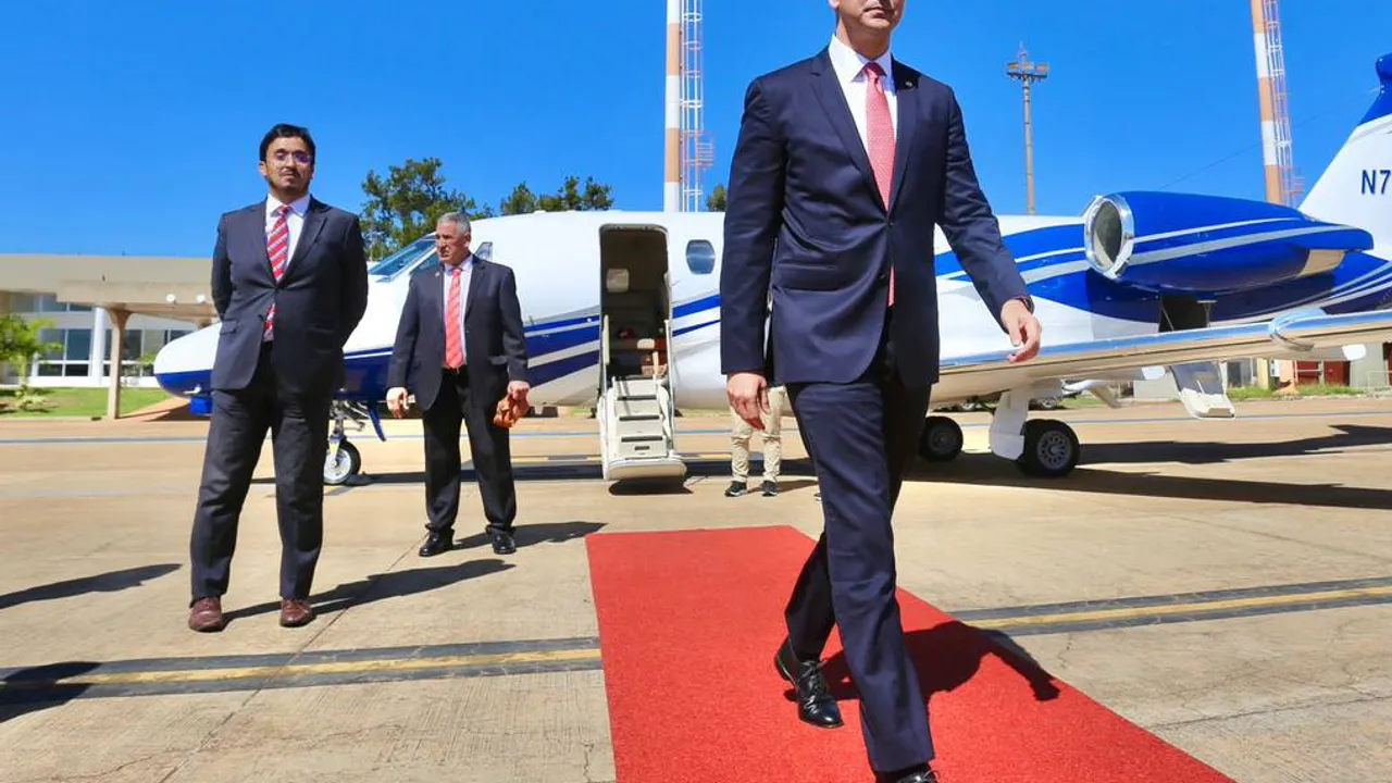Comitiva presidencial caminando sobre una alfombra roja en la pista cerca de una aeronave ejecutiva blanca.