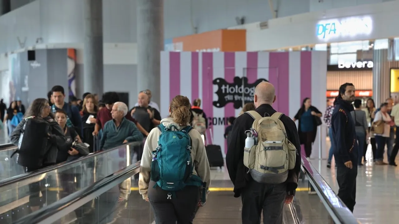 Pasajeros con mochilas y equipaje caminan por un pasillo dentro de la terminal del aeropuerto internacional.