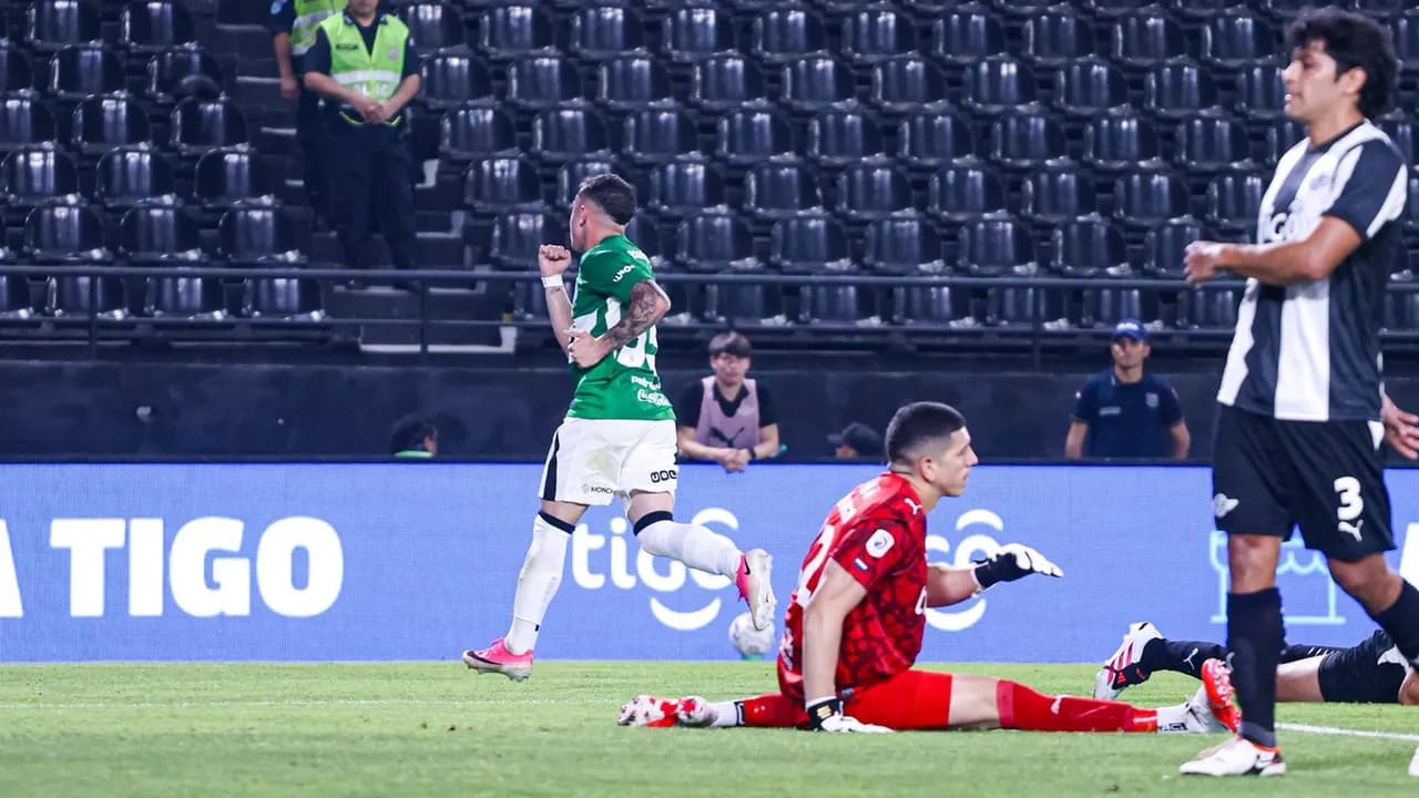Futbolista festeja el gol mientras el arquero rival permanece sentado sobre el césped durante el partido.