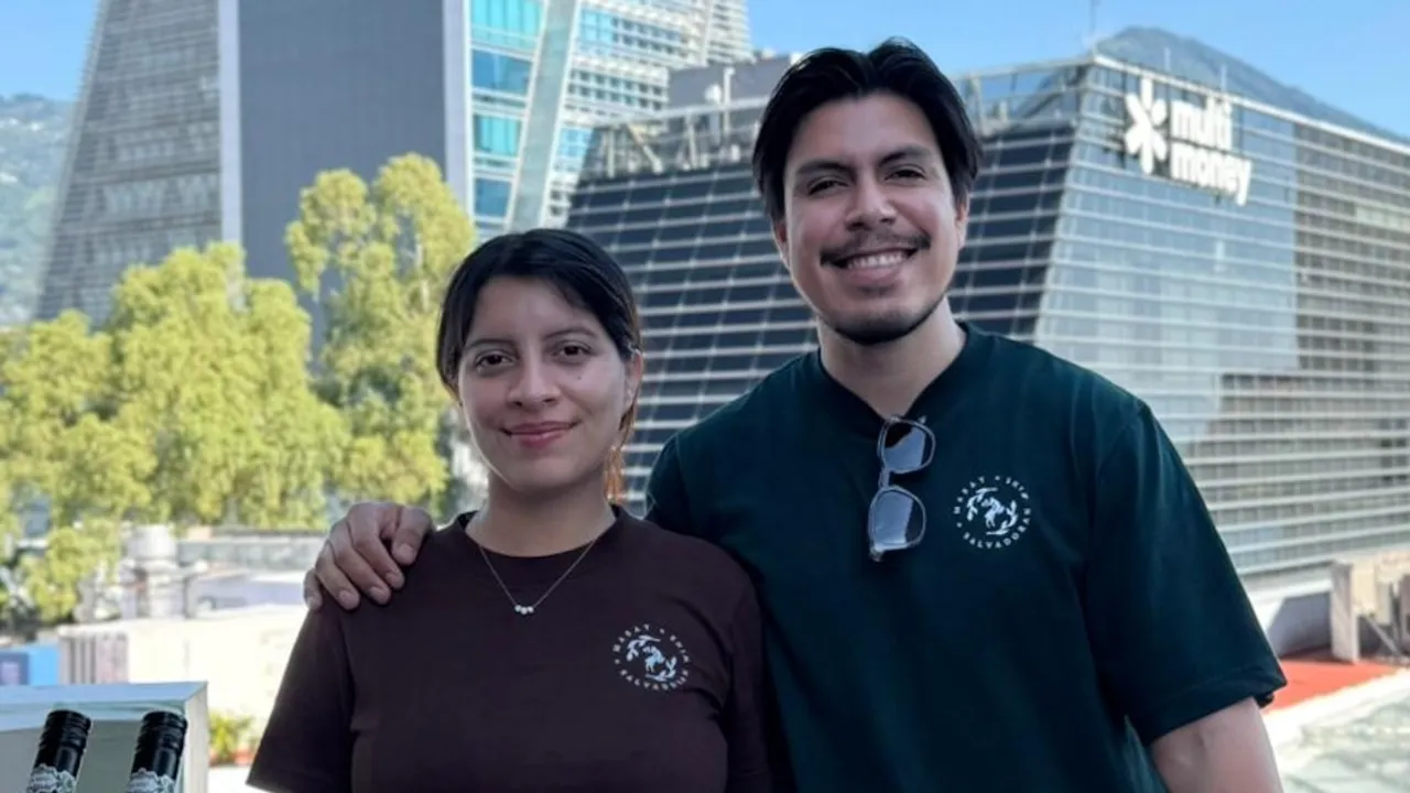 Hombre y mujer sonrientes con remeras oscuras del emprendimiento Masat frente a edificios corporativos