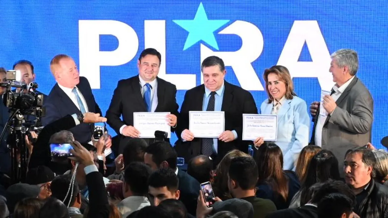 Autoridades del partido liberal sostienen diplomas en el escenario frente a un panel azul con la sigla PLRA