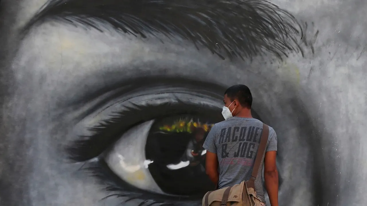 Hombre con mascarilla camina frente a una pared con un mural artístico de un ojo gigante en blanco y negro.