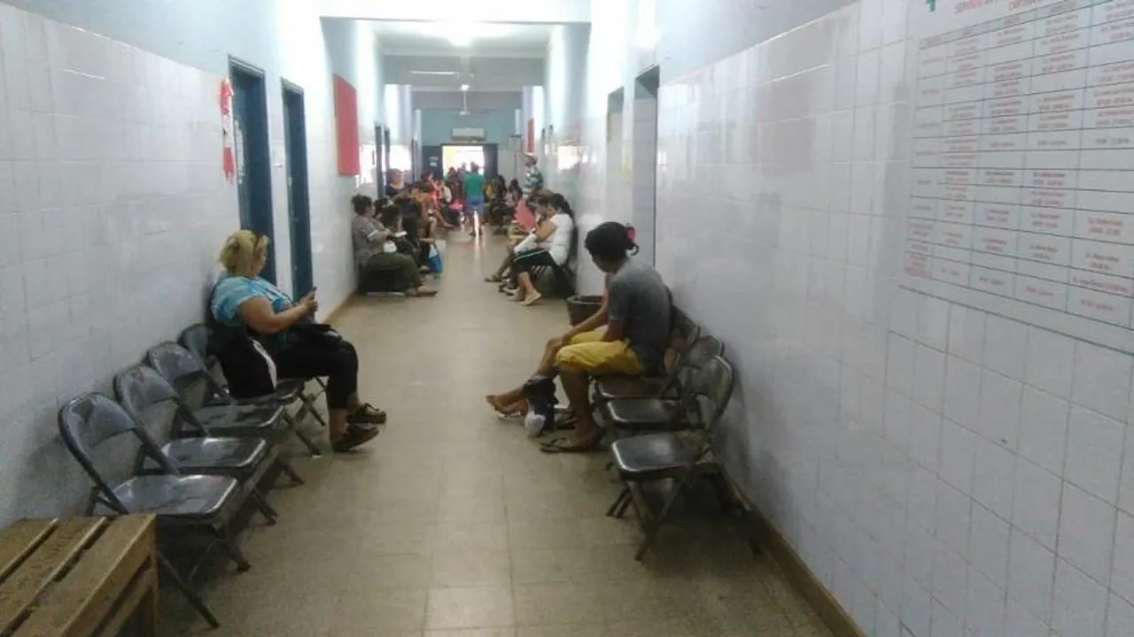 Pasillo de un centro de salud con personas sentadas en sillas plegables esperando atención médica.