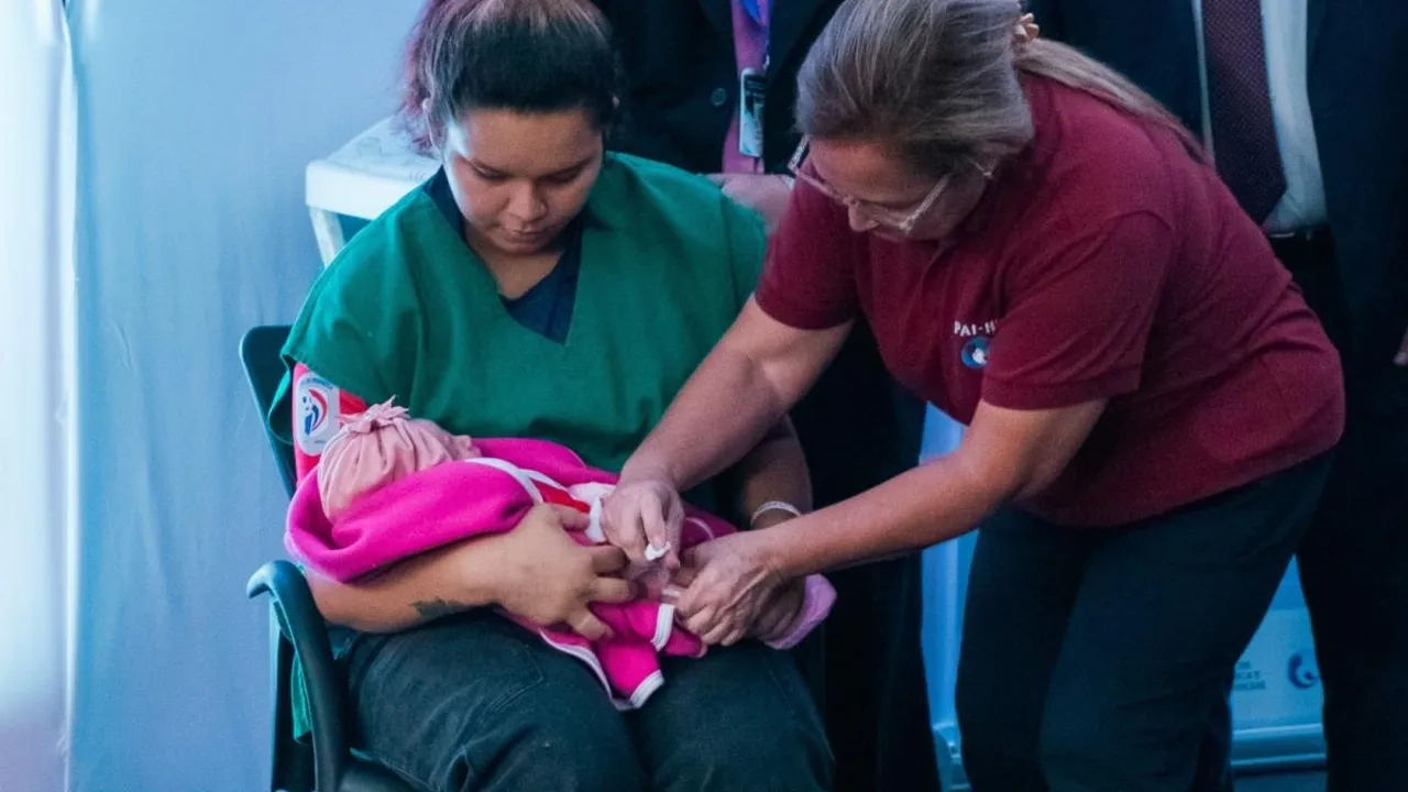 Una enfermera aplica una inyección en el brazo de un bebé en brazos de su madre durante una vacunación.