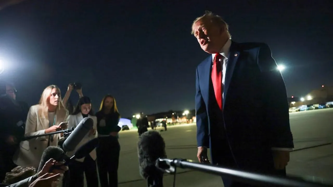 Donald Trump habla frente a micrófonos de prensa en una pista de aterrizaje durante la noche.