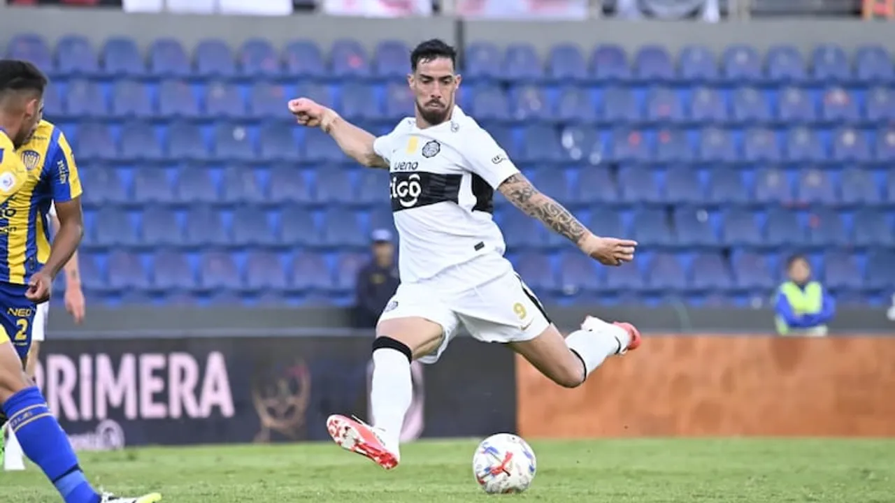 Un futbolista con la camiseta blanca del club Olimpia pateando un balón durante un partido en la cancha.