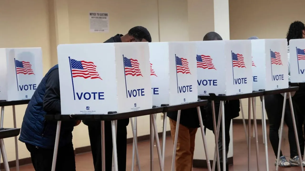 Ciudadanos votando en cabinas electorales individuales adornadas con banderas de Estados Unidos y la palabra vote.
