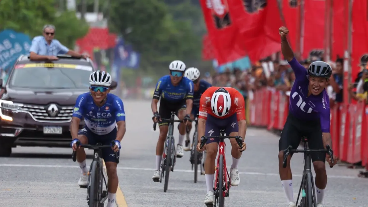 Ciclistas cruzan la línea de meta al sprint final, mientras uno de ellos viste de morado y alza el puño en victoria.